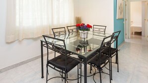 A dining area with a glass table and black metal chairs, a vase with red flowers, and a modern pendant light. - Cosy apartment for 6 guests with A/C, pool, WIFI, TV and terrace (Castell-platja D'aro)