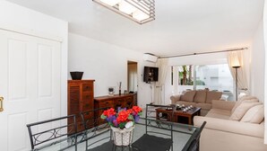 A modern living room with a glass dining table, a sofa, and a TV. - Cosy apartment for 6 guests with A/C, pool, WIFI, TV and terrace (Castell-platja D'aro)