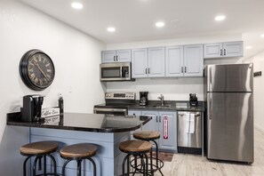 Una cocina moderna con una isla central, taburetes de bar, electrodomésticos de acero inoxidable y un reloj en la pared.