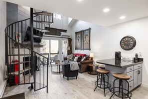 Una cocina moderna con barra, una escalera de caracol y una sala de estar con sofá y bar de café.