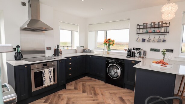 A modern kitchen with a built-in oven, microwave, and washing machine. - Park Cottage (Isle of North Uist)