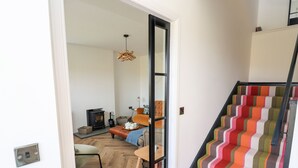 A staircase with colorful striped carpeting leading to a room with a wooden floor, a sofa, and a small table with a teapot. - Park Cottage (Isle of North Uist)