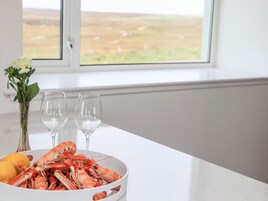 Una mesa con un plato de langosta cocida, dos copas de vino vacías, un florero con flores y un limón.