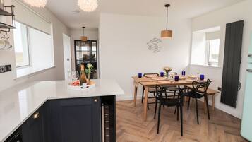 A modern kitchen with a dining area, wooden herringbone flooring, and pendant lighting.