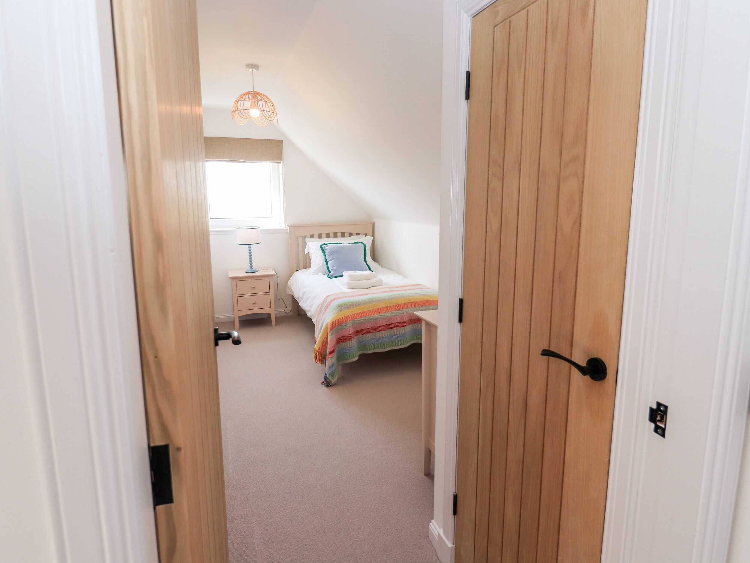 A bedroom with a bed, bedside table, lamp, and a hanging light fixture.
