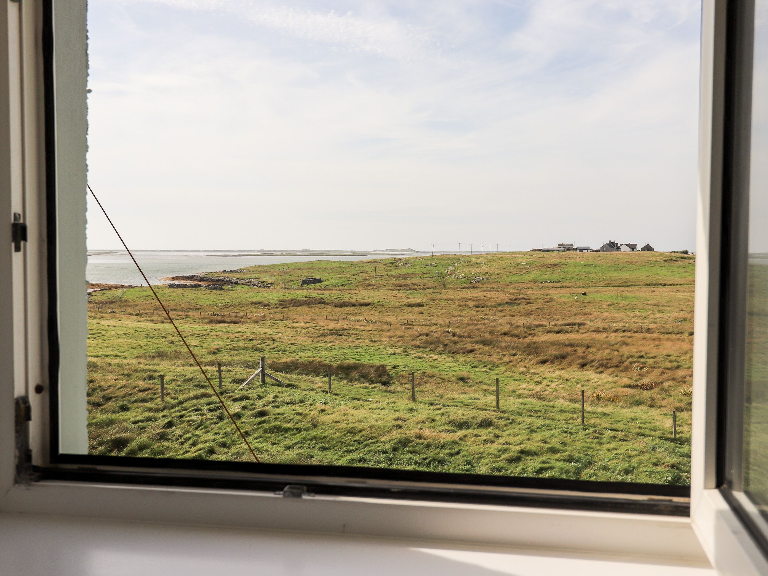 A view from a window of a grassy field with a body of water in the distance and a few buildings.