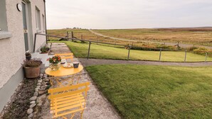 A patio with a table and chairs, a small garden, and a view of a rural landscape. - Park Cottage (Isle of North Uist)