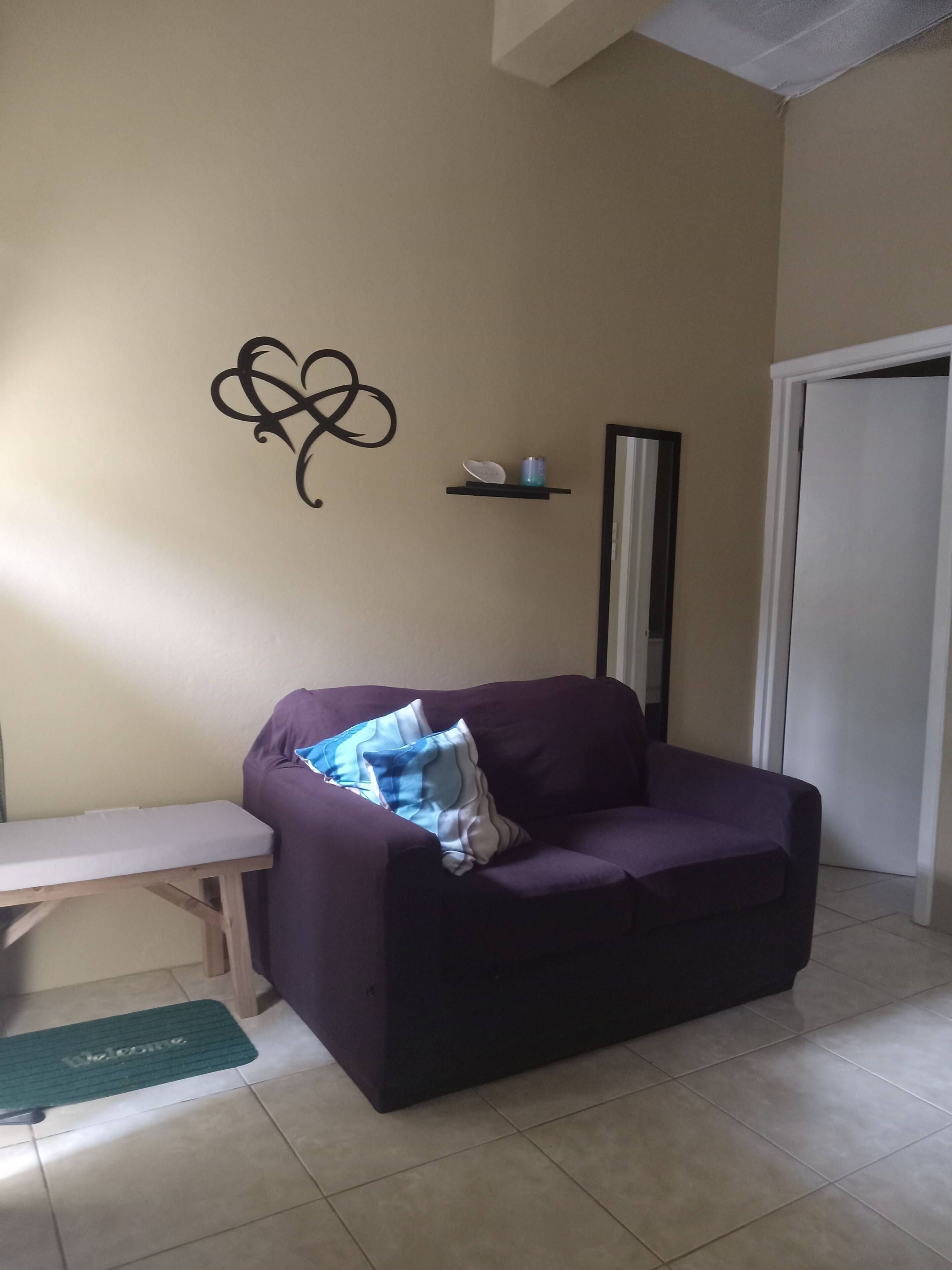A living room with a purple sofa, a small table, a decorative wall piece, and a white door.
