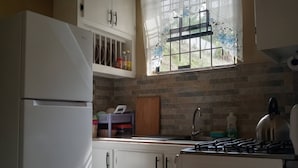 A compact kitchen with white cabinets, a built-in gas stove, and a window with a floral curtain. - Near Ferry, Airport, Shops, Beaches, Atms, Rodney Bay and Castries - Free Pickup (Castries)