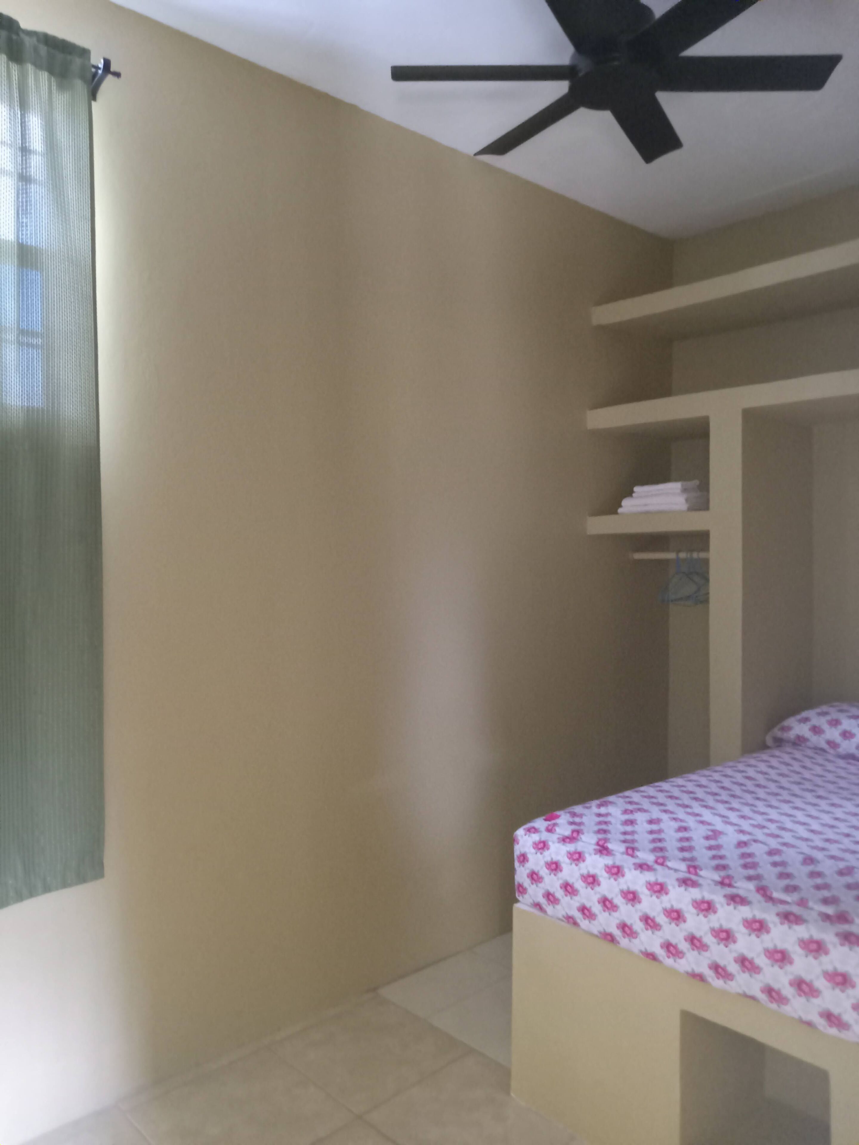 A bedroom with a bed, a ceiling fan, and a window with a curtain.