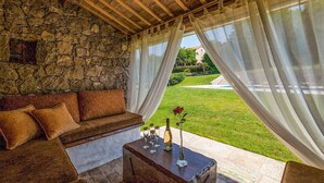 A cozy room with a stone wall, a wooden ceiling, and a view of a well-maintained lawn and building in the background. - Beautiful home in Buzet (Buzet)