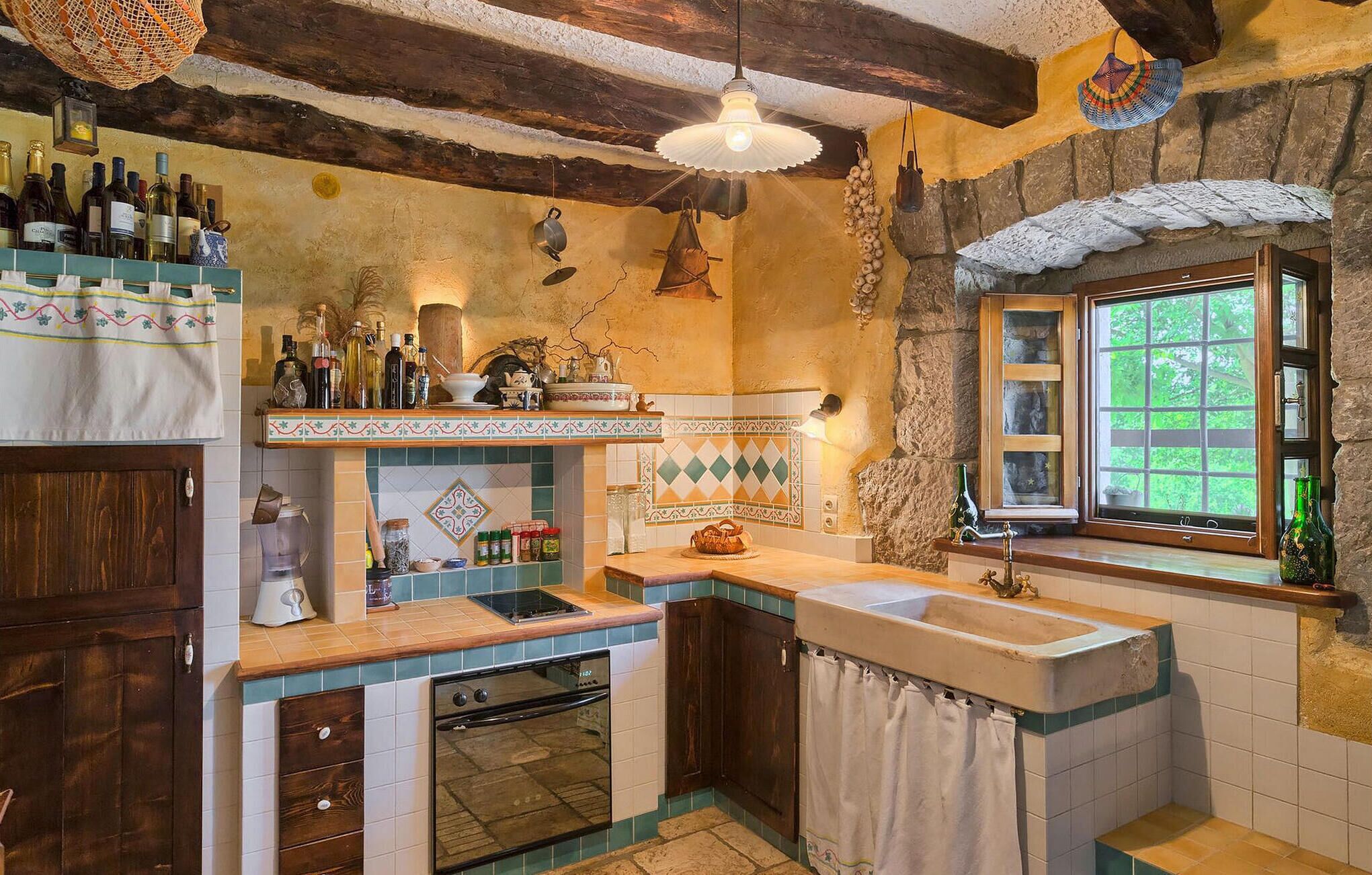 Una cocina rústica con techo de madera, pared de piedra y ventana con vistas a la vegetación.