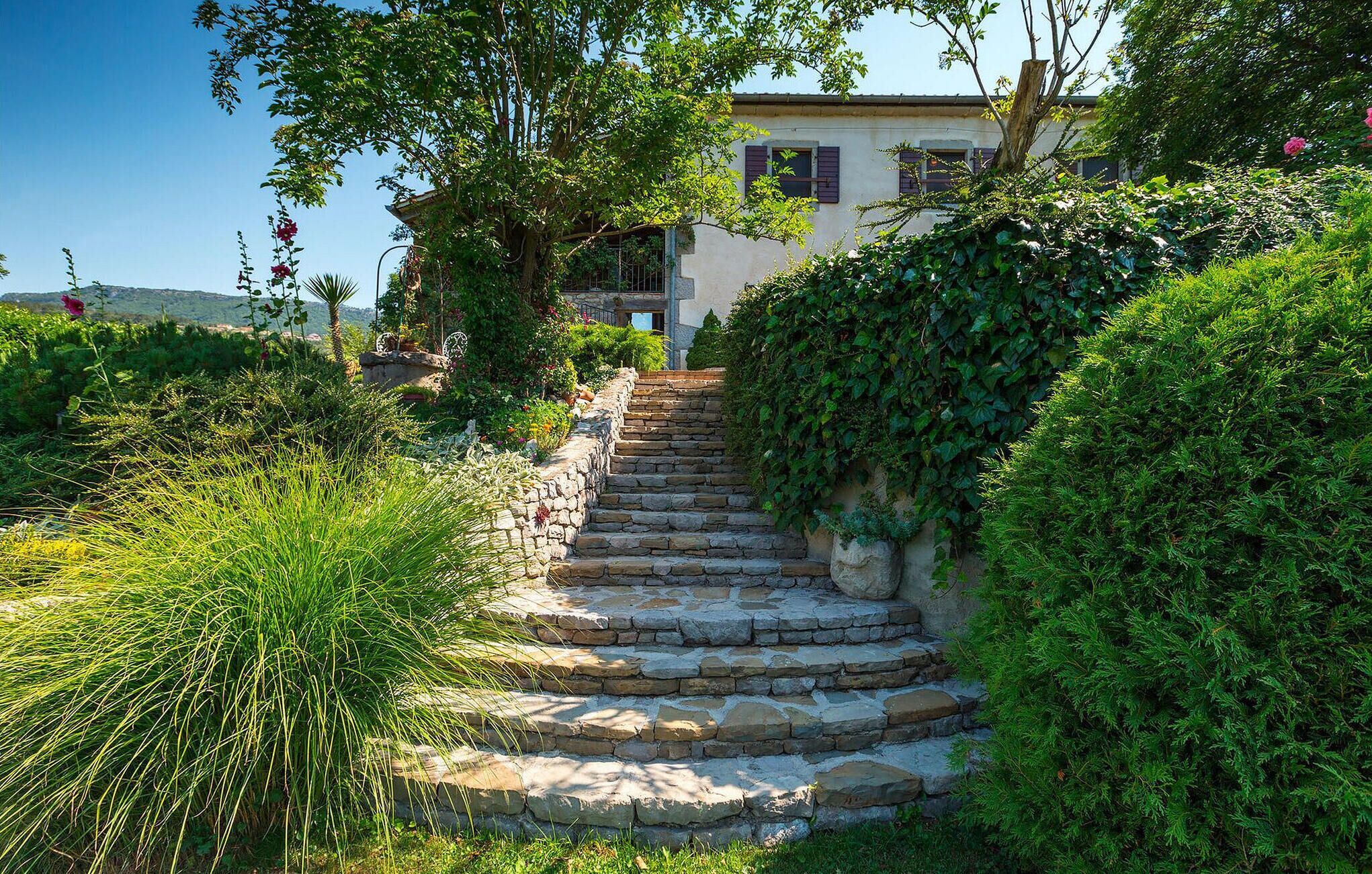 A stone staircase leading to a house surrounded by lush greenery and flowering plants.