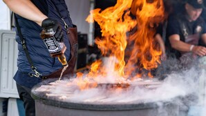 A person pouring a liquid onto a fire, with flames and smoke visible.
