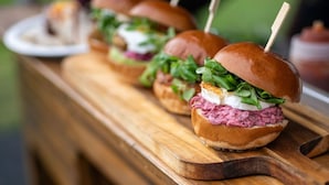 A wooden table with a row of sandwiches, each with a toothpick.