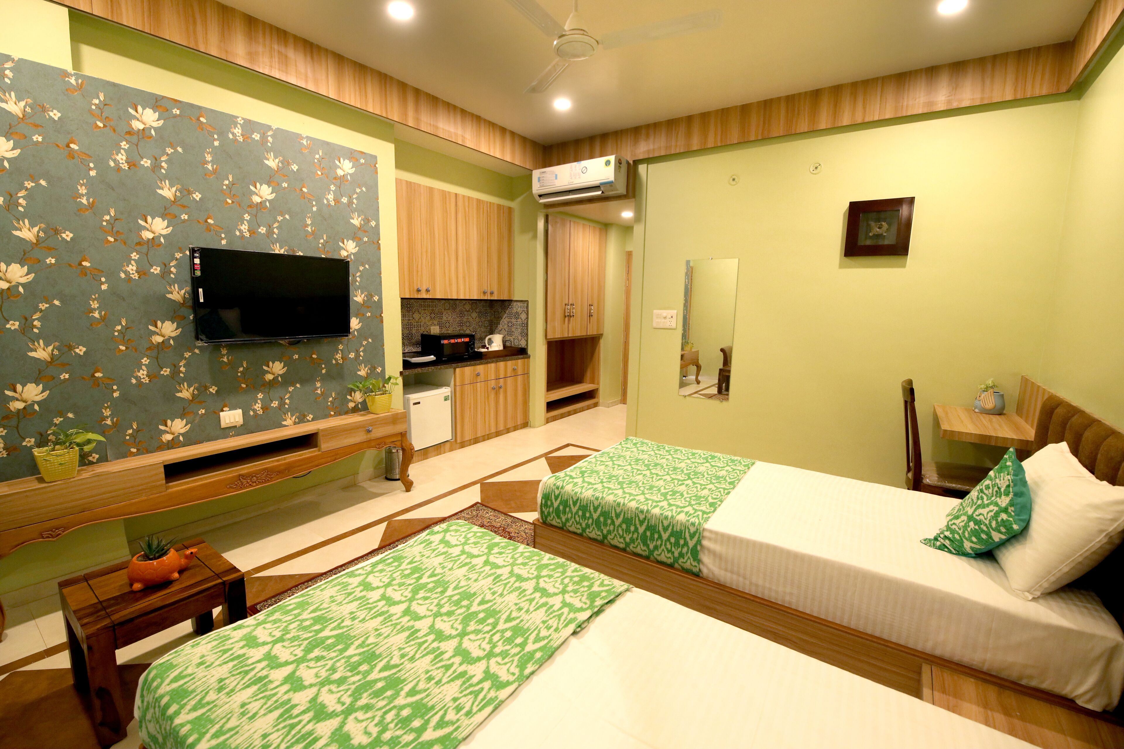 A hotel room with two beds, a TV, a small kitchenette, and a bathroom.