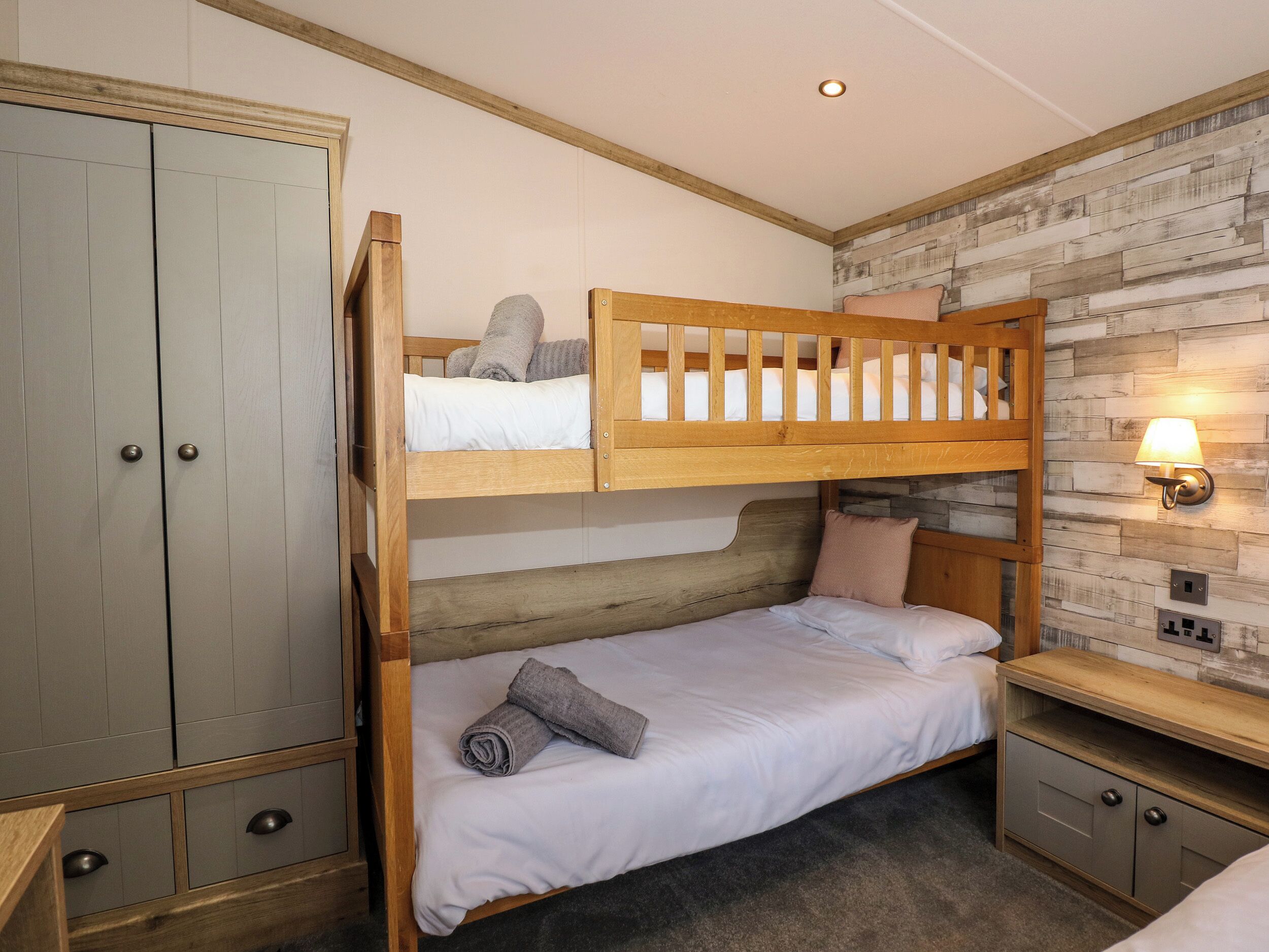 Une chambre avec un lit superposé, une armoire, une table de chevet et une lampe fixée au mur.