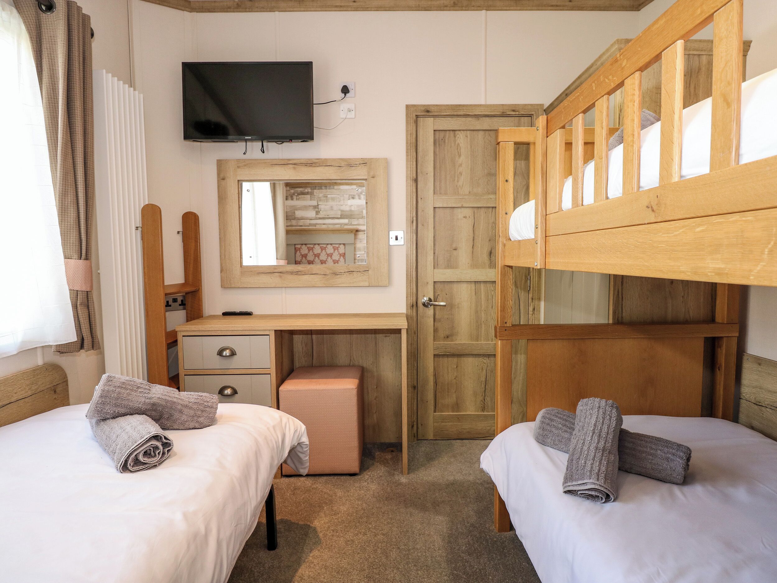 Ein Schlafzimmer mit zwei Betten, einem Schreibtisch, einem Fernseher und einer Holztür.
