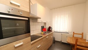 Una cocina moderna con horno empotrado, armarios de madera, extractor de acero inoxidable y una ventana con cortinas de gasa.