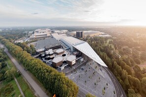 An aerial view of a modern building complex with multiple structures, surrounded by greenery and a parking area. - Holiday Home in Essen with Balcony Views (Essen)