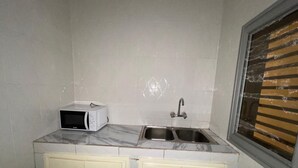 A small kitchen with a microwave, two sinks, and light-colored cabinets. - Residence in Tounkaranké (Bamako)