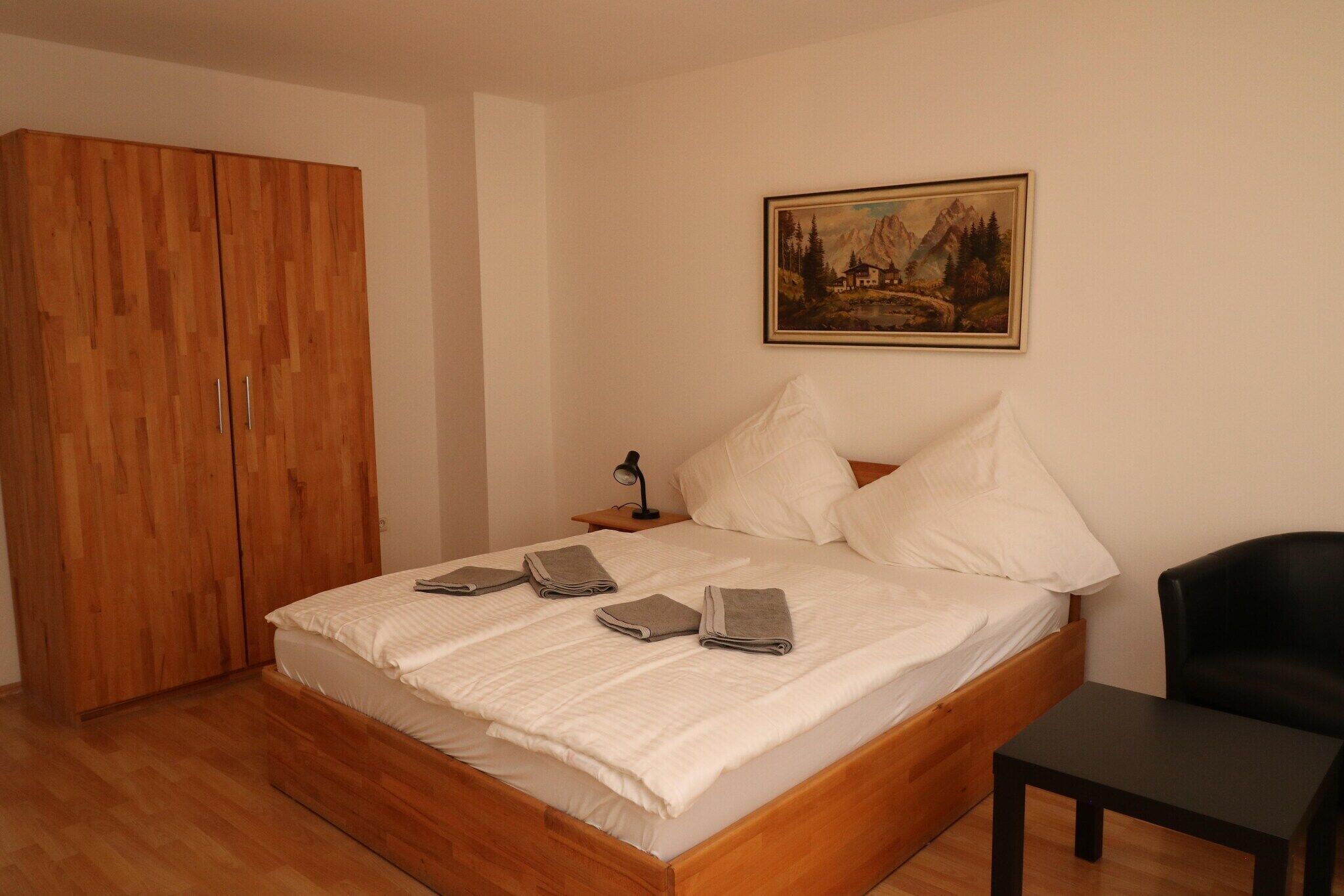 A bedroom with a wooden bed, a black chair, a nightstand with a lamp, and a painting on the wall.