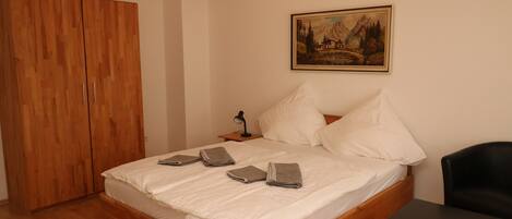 A bedroom with a wooden bed, a black chair, a nightstand with a lamp, and a painting on the wall.
