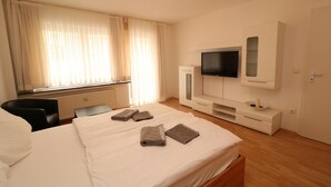 A hotel room with a bed, a TV, a desk, and a window with curtains. - Rustic Apartment in Essen (Essen)