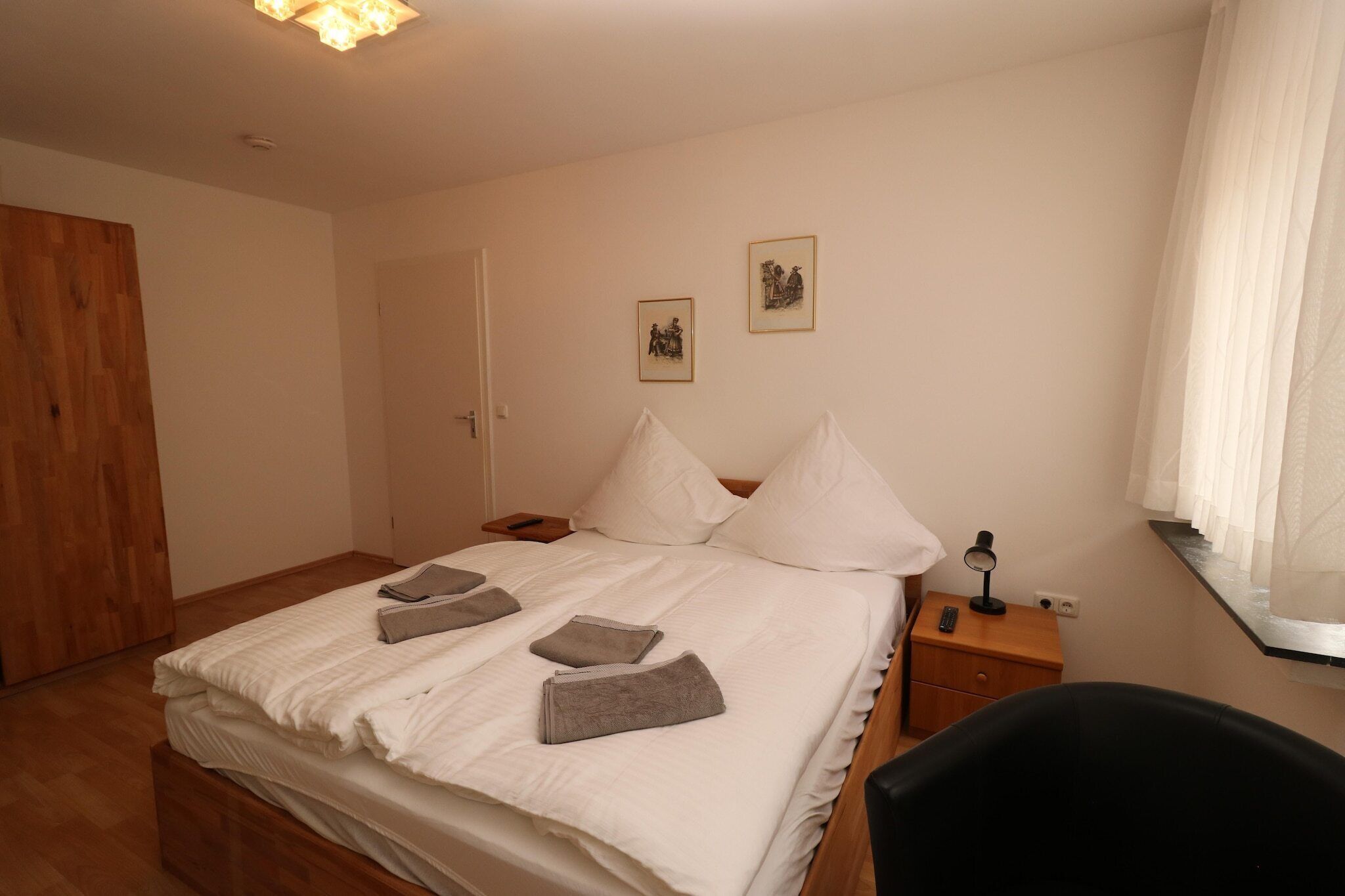 A neatly made bed with pillows and towels, a bedside table with a lamp, and a wooden wardrobe.