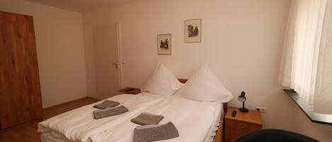 A neatly made bed with pillows and towels, a bedside table with a lamp, and a wooden wardrobe.