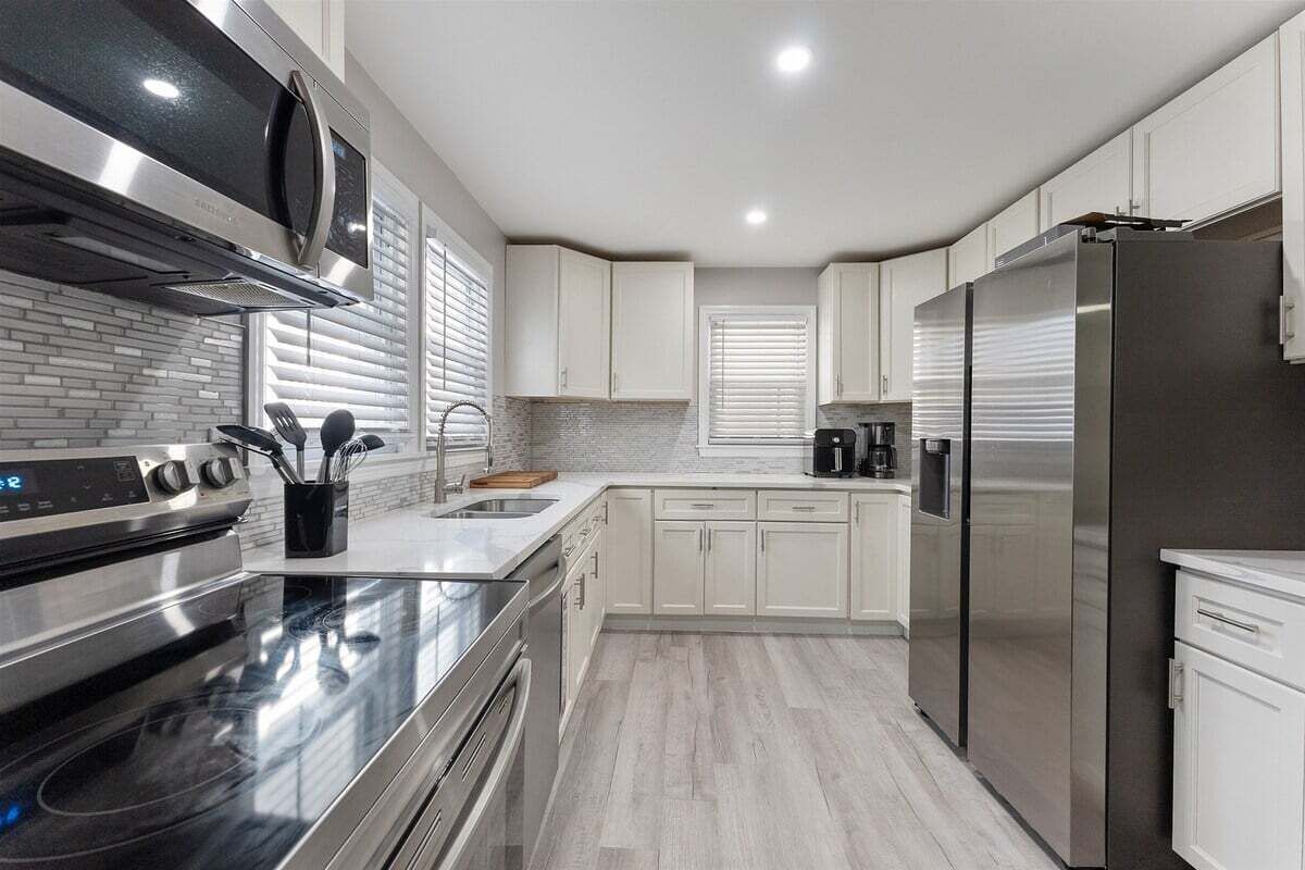 A modern kitchen with stainless steel appliances, white cabinetry, and a tiled backsplash.