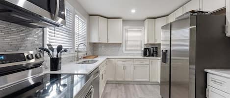 Cocina moderna con electrodomésticos de acero inoxidable, armarios blancos y salpicadero de azulejos.