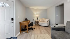 A compact living space with a desk, office chair, sofa, and a grey armchair. - Modern 2BR Condo Walk to Beach and Dining (Wildwood)