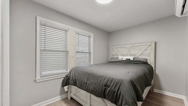 A bedroom with a bed, white window blinds, a white headboard, and a ceiling light. - Modern 2BR Condo Walk to Beach and Dining (Wildwood)