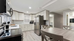 A modern kitchen with white cabinetry, stainless steel appliances, and a wooden dining table. - Modern 2BR Condo Walk to Beach and Dining (Wildwood)