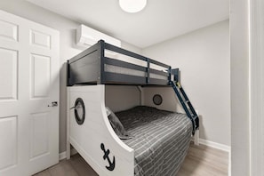 A bunk bed with a ladder, a circular window, and a door in a room with white walls and a light-colored floor.