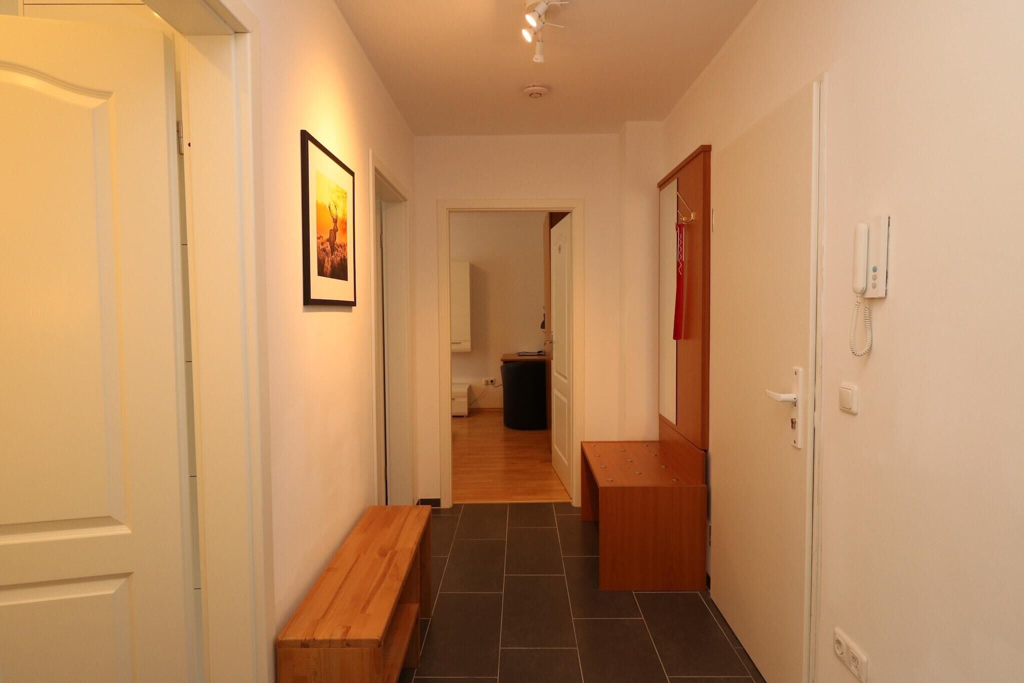 A narrow hallway with a wooden bench, a framed picture on the wall, and a door on the right.