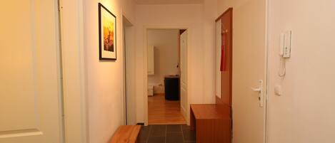 A narrow hallway with a wooden bench, a framed picture on the wall, and a door on the right.