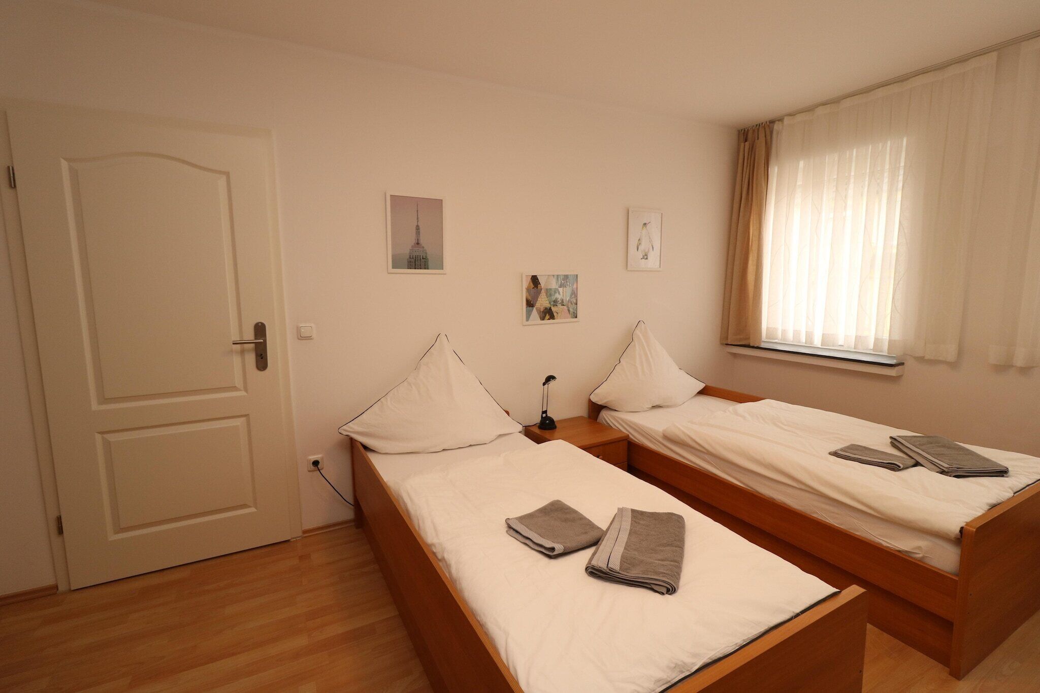 Ein Zimmer mit zwei Einzelbetten, einer Tür und einem Fenster mit Vorhängen.