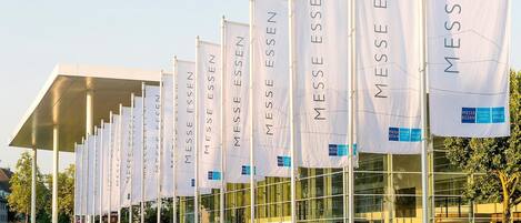 Un edificio moderno con varias banderas blancas que muestran 'MESSE ESSEN' y 'HALL MESSE ESSEN'.