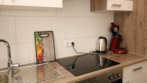 Une cuisine moderne dotée d’un évier en acier inoxydable, d’une plaque de cuisson à induction noire, d’une bouilloire rouge et d’une planche à découper en bois sur laquelle se trouvent des légumes.