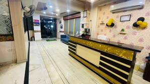 A reception area with a marble floor, a reception desk with a black and gold design, and a wall-mounted air conditioner. - Hotel Alpine By The Golden Taj Group (Agra)