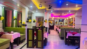 A restaurant with booths and tables, some with pink tablecloths. - Hotel Alpine By The Golden Taj Group (Agra)