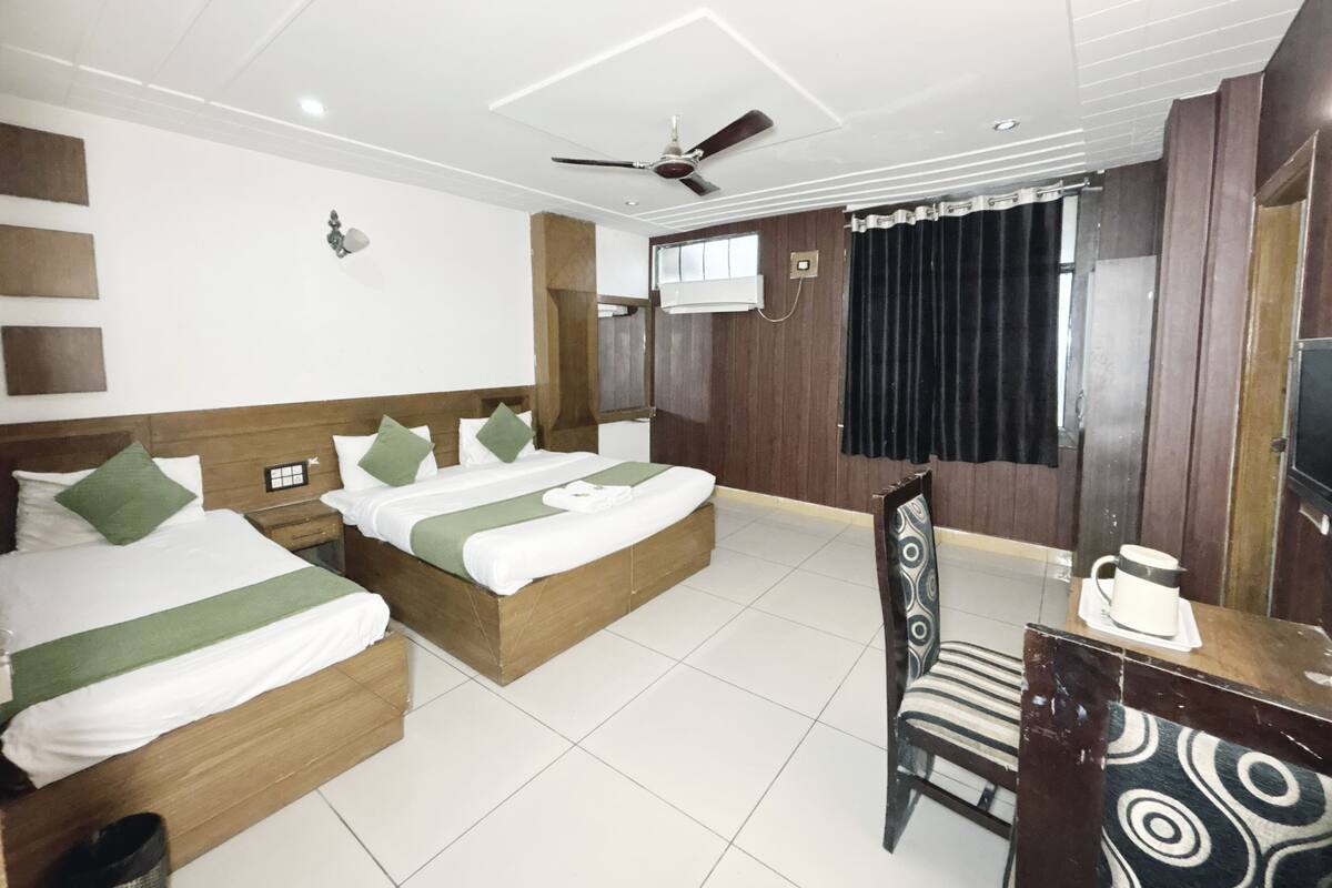 Une chambre d’hôtel avec deux lits, un bureau, une chaise, un ventilateur de plafond et un appareil de climatisation.