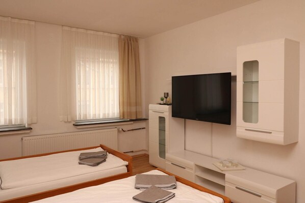 A hotel room with two beds, a TV, a minibar, and a window with curtains. - Stylish Essen Apartment Balcony Cityview (Essen)