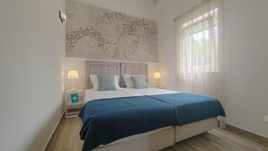Une chambre à coucher comprenant un lit, deux tables de chevet, une œuvre d’art murale et une fenêtre avec des rideaux.