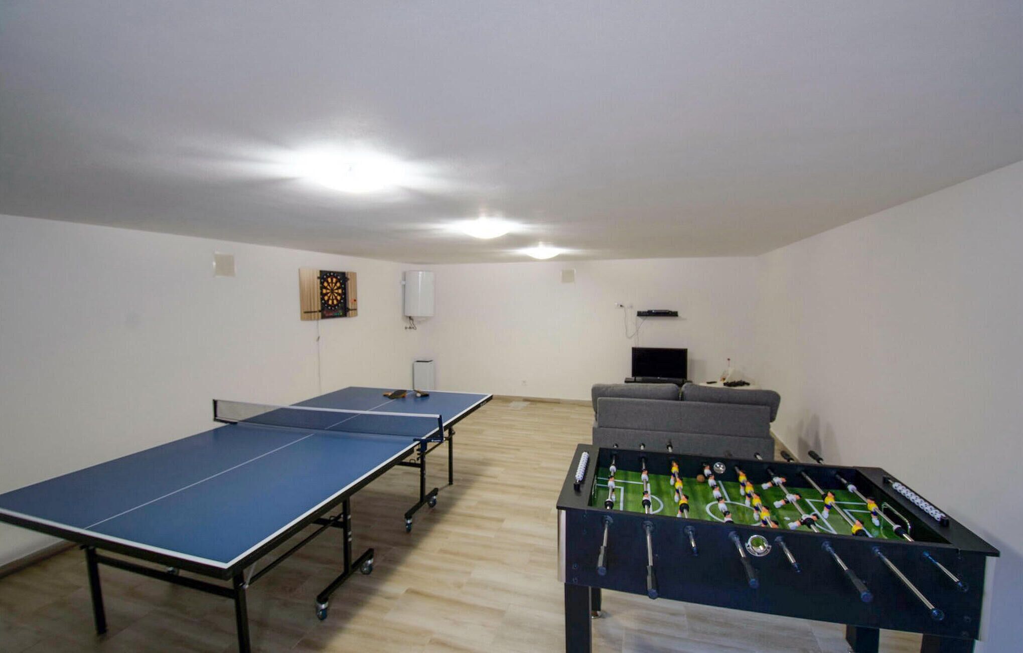 Ein Raum mit Tischtennisplatte, Kicker, grauem Sofa und Fernseher.
