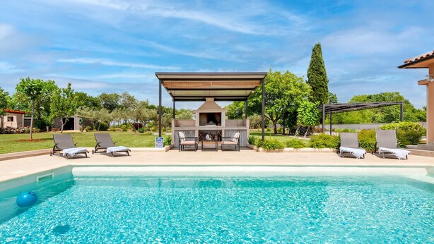 Une piscine avec des chaises longues et un espace barbecue.