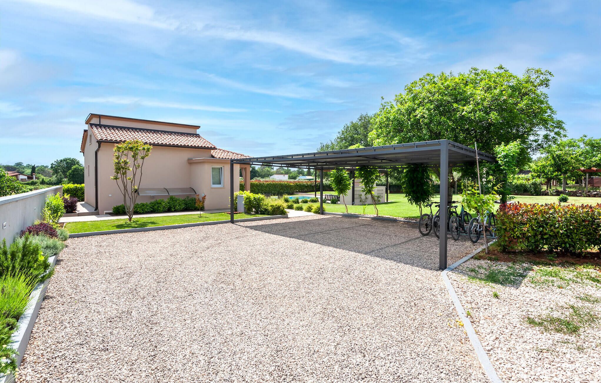 A covered outdoor area with a gravel patio, a pergola, and a building with a tiled roof.