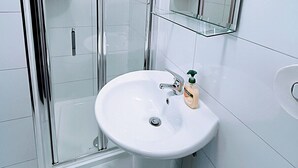 Uma casa de banho moderna com cabine de chuveiro em vidro, uma pia branca e um espelho.